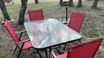 A square table with four red chairs in an outdoor setting with trees and a shed in the background.