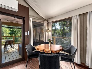 Una habitación con una mesa redonda de madera, sillas de mimbre negro, vistas a una terraza y un ventanal con cortinas.