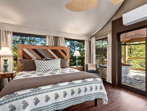 Un dormitorio con una cama grande, cabecera de madera y vistas a un jardín a través de amplios ventanales.