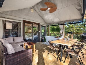 Un espacio al aire libre con carpas, un sofá, una mesa de comedor, sillas y una parrilla.