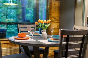 Ein runder Esstisch mit einer Vase orangefarbener Tulpen, blauen Tellern und Weingläsern.