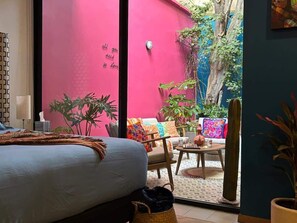 A bedroom with a bed, a small table, and chairs, a window, and a pink wall.