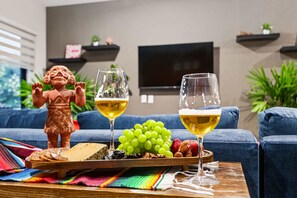 Ein Wohnzimmer mit einem blauen Sofa, einem Couchtisch aus Holz mit einer Platte voller Snacks, zwei Weingläsern und einer dekorativen Figur.