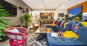 Ein modernes Wohnzimmer mit einer Couch, bunten Stühlen, einem Couchtisch und einer Küche im Hintergrund.