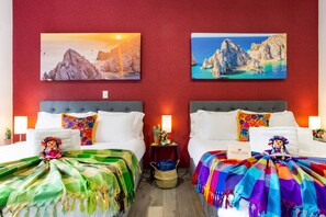 Ein Hotelzimmer mit zwei Betten, farbenfrohen Kissen, einem Kaktus und Bildern an den Wänden.