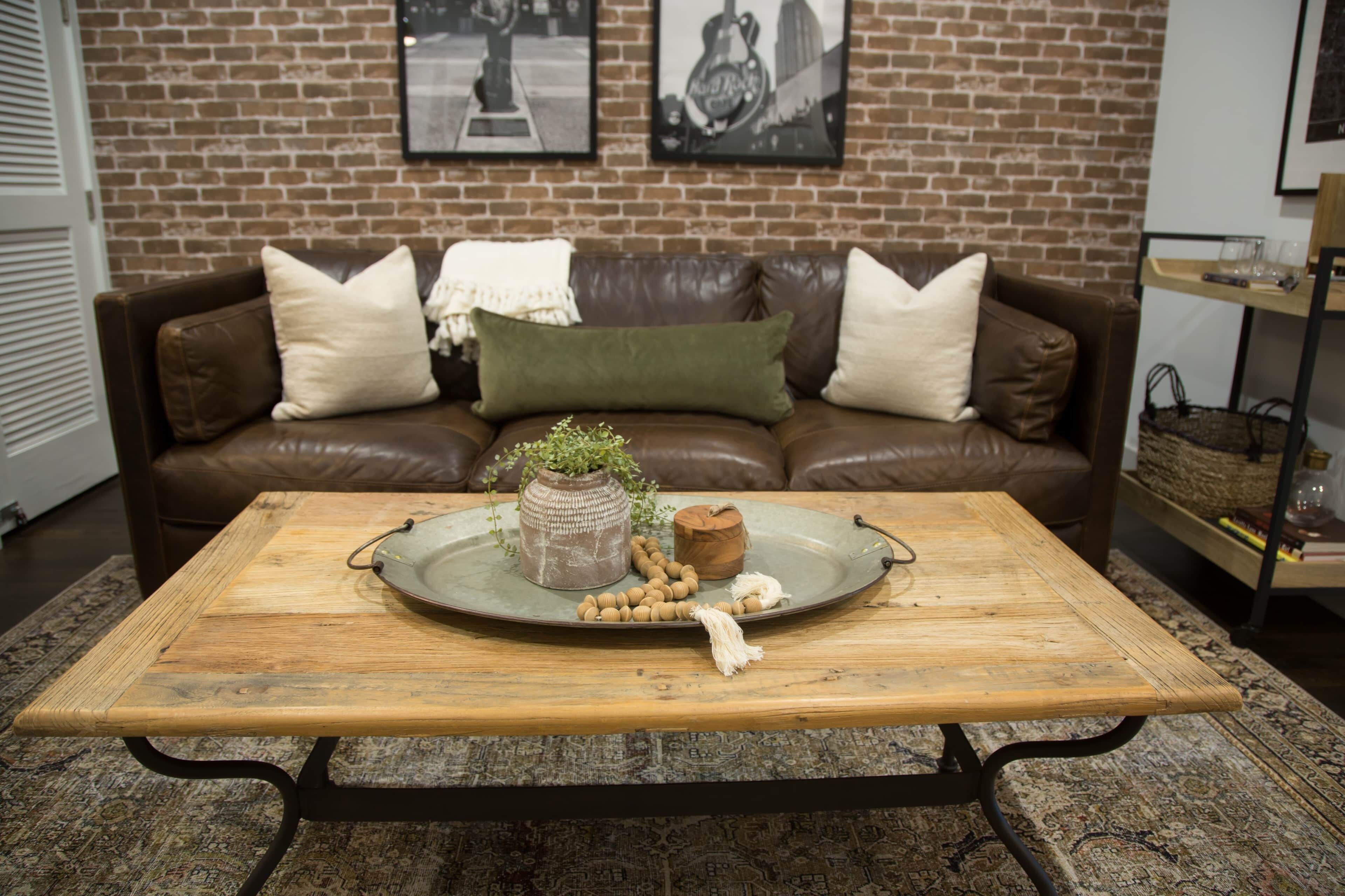 A living room with a brown leather couch, a wooden coffee table, and a brick wall with two framed pictures.
