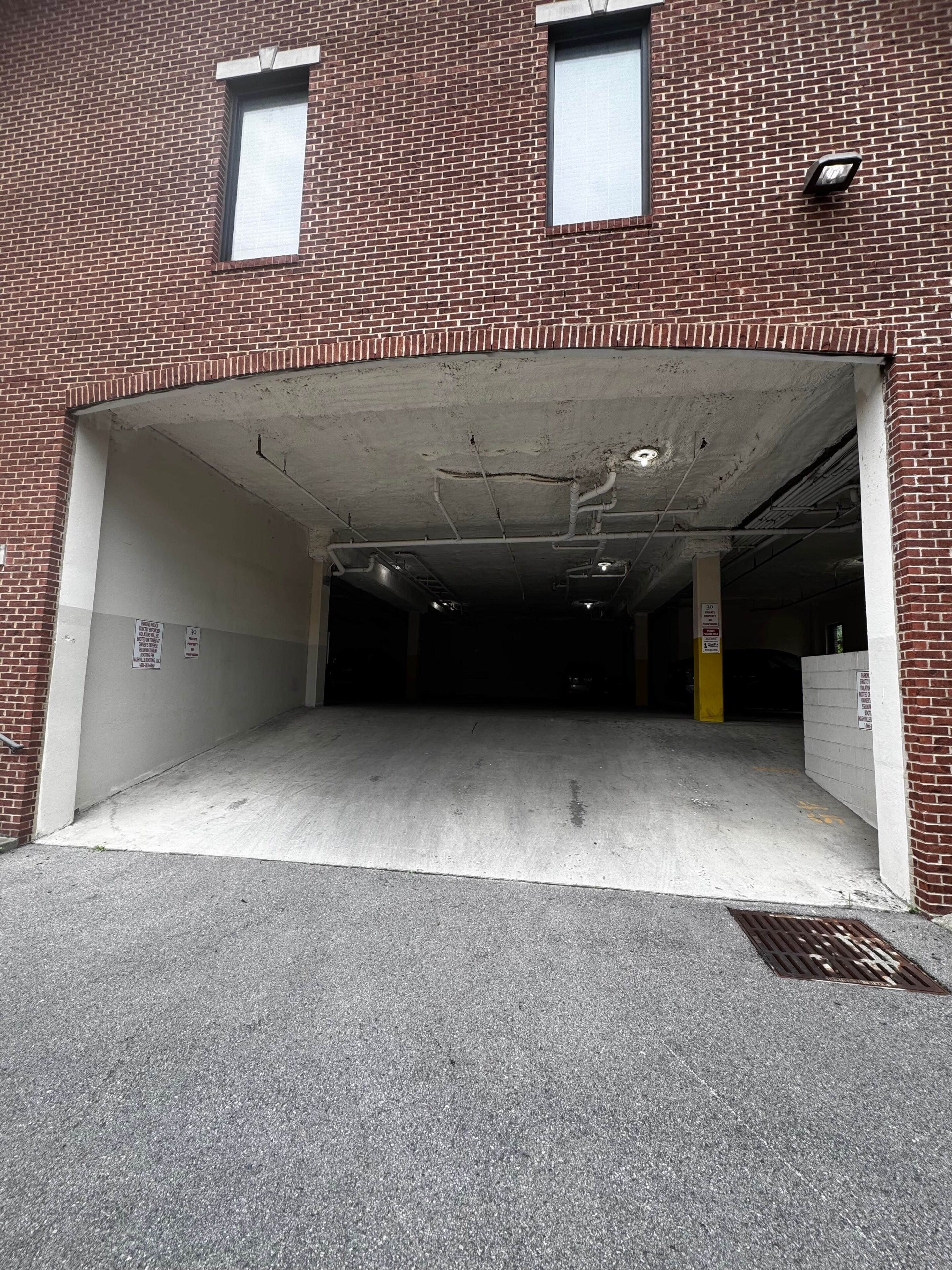 A brick building with a garage entrance, concrete floor, and visible pipes on the ceiling.