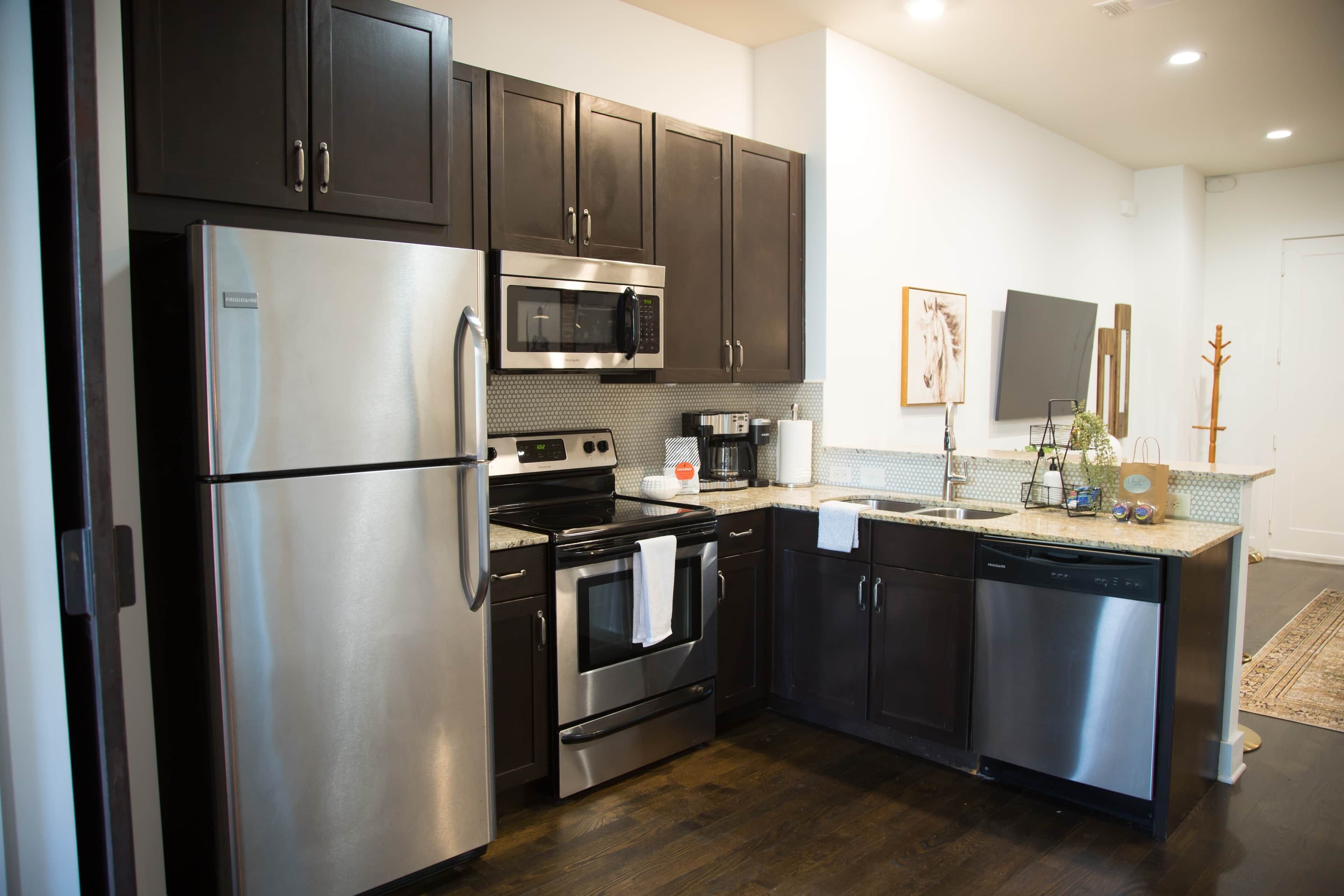 A modern kitchen with stainless steel appliances, dark cabinetry, and a tiled backsplash.