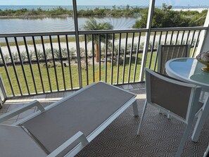 Een balkon met uitzicht op een meer, een tafel met stoelen en een klein vloerkleed.