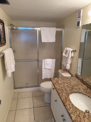 Een badkamer met een douchecabine van glas, een toilet, een wastafel met een granieten blad en een spiegel.