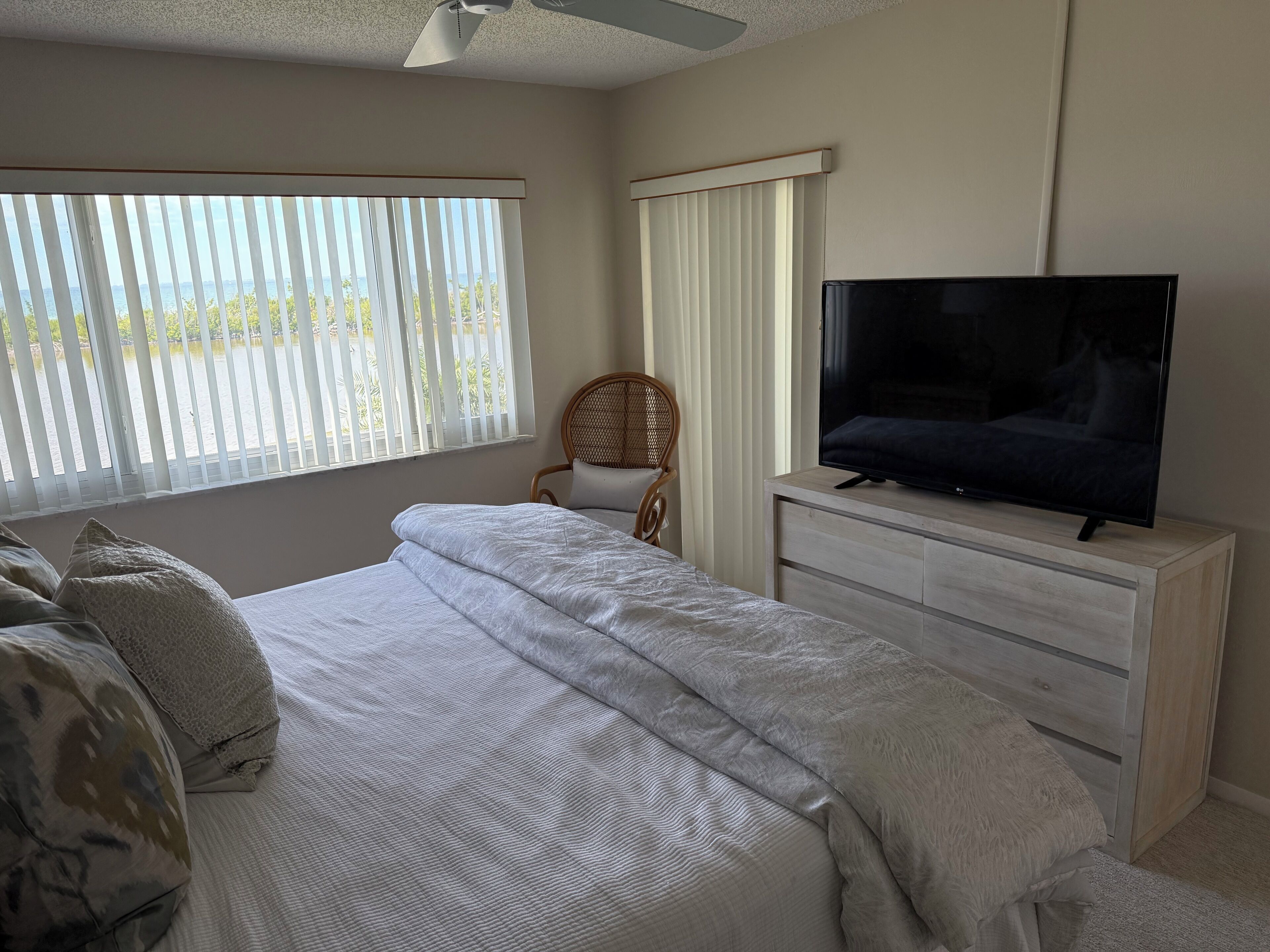Une chambre à coucher avec un lit, un téléviseur posé sur une commode, une chaise et une vue sur l’extérieur par la fenêtre.