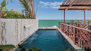 Piscina con vista al océano, rodeada de plantas tropicales y una terraza de madera.