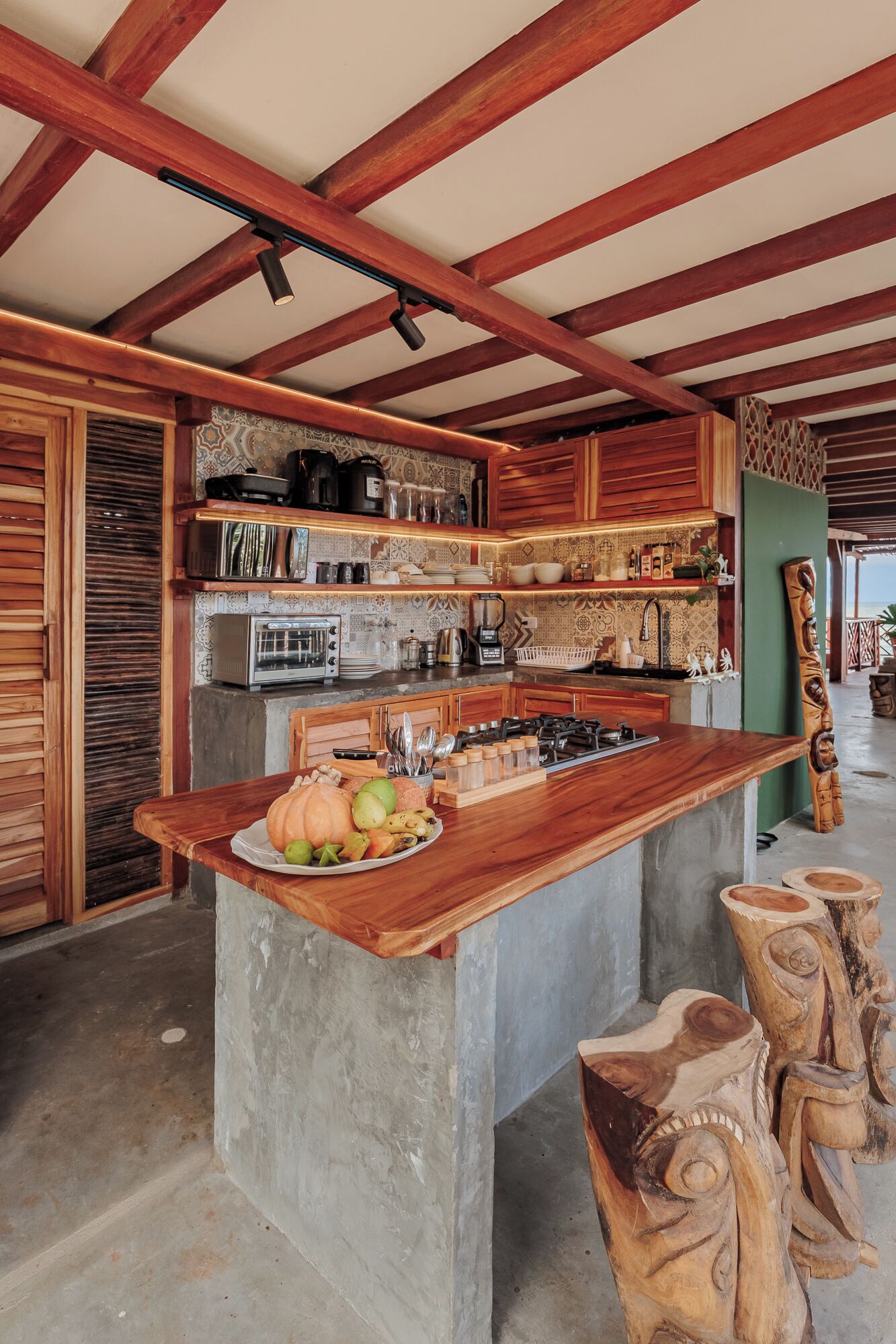 A kitchen with a central island, wooden beams, and a green wall.
