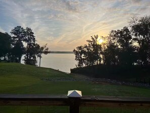 Une vue d’un lac au coucher du soleil, avec des arbres et une zone herbeuse.