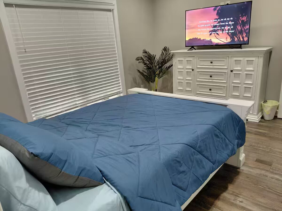 A bedroom with a bed, a TV on a cabinet, and a window with blinds.