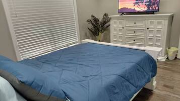 A bedroom with a bed, a TV on a cabinet, and a window with blinds.