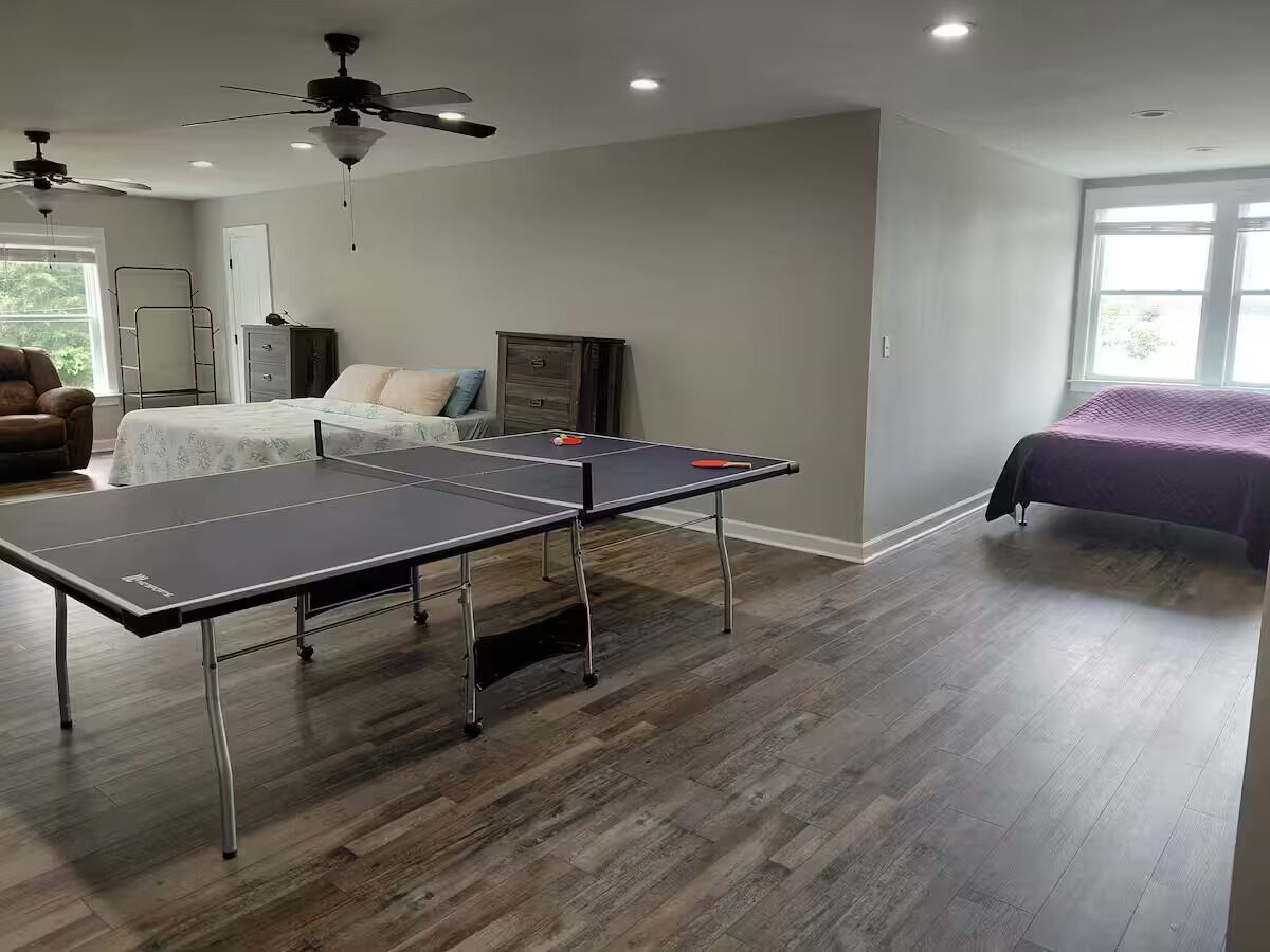 A room with a ping pong table, a bed, a wardrobe, and a ceiling fan.