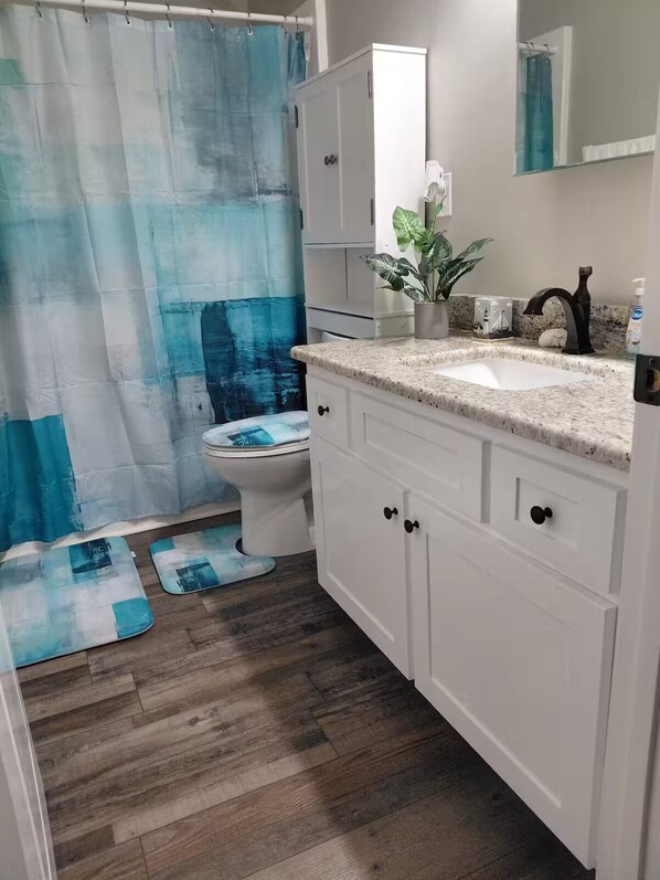 Une salle de bain avec un rideau de douche, des toilettes, un lavabo, des placards et une plante en pot.
