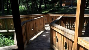 Een houten terras met leuningen en decoratieve uitsnijdingen, omringd door groen.