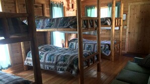 Een slaapkamer met stapelbedden, houten wanden en vloeren, een groene bank en een raam met gordijnen.