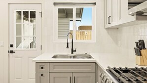 Una cocina con un lavamanos de acero inoxidable, una ventana que ofrece vistas a una terraza de madera, y una estufa con un bloque de cuchillos.