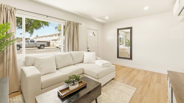Una sala moderna con un sofá modular, una mesa de centro con una planta, un espejo grande y vista a la calle.