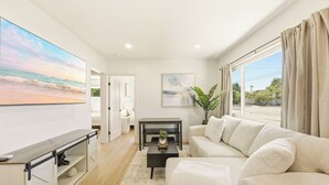 Una sala de estar moderna con un sofá, una mesa de centro, televisor y vista a la playa.