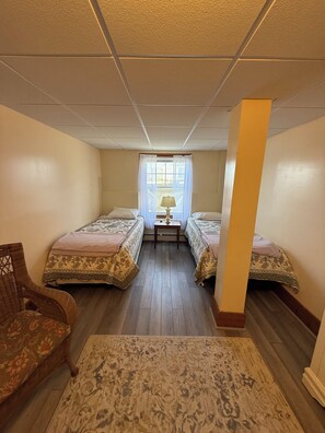 A room with two beds, a small table with a lamp, a chair, and a window with curtains. - Beachfront 2-Bedroom Apartment on Wells Beach Sleeps 6 (Wells)
