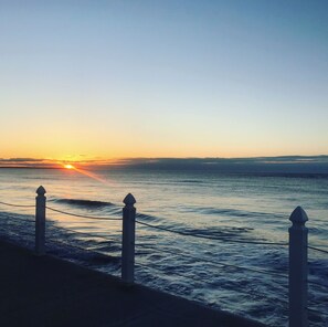 Pôr do sol sobre o oceano, com um corrimão em primeiro plano.