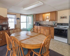A kitchen with a dining table, chairs, a stove, and cabinets. - Beachfront 2-Bedroom Apartment on Wells Beach Sleeps 6 (Wells)