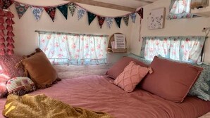 Une chambre à coucher avec un lit, des oreillers, une couverture, des rideaux à motifs floraux et une étagère fixée au mur.