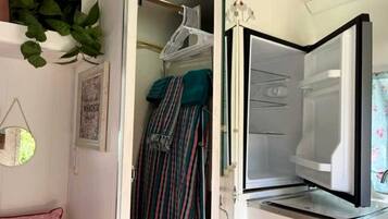 A room with a bed, a hanging plant, a mirror, and a closet with hanging clothes.