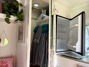 Una habitación con cama, una planta colgante, un espejo y un armario con ropa colgada.