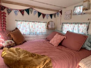 Une chambre à coucher avec un lit, des oreillers, une couverture, des rideaux à motifs floraux et une étagère fixée au mur.