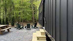 A cabin with a gravel patio, wooden benches, and Adirondack chairs.