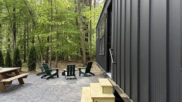 A cabin with a gravel patio, wooden benches, and Adirondack chairs.