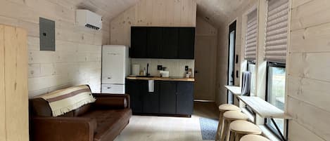 Cocina compacta con isla central, sofá y barra con taburetes.