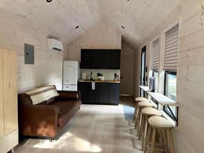 A compact kitchen with a central island, a sofa, and a bar area with stools. - Nordic-Inspired Tiny Cabin Near Lake George & Hudson River, New York (Corinth)