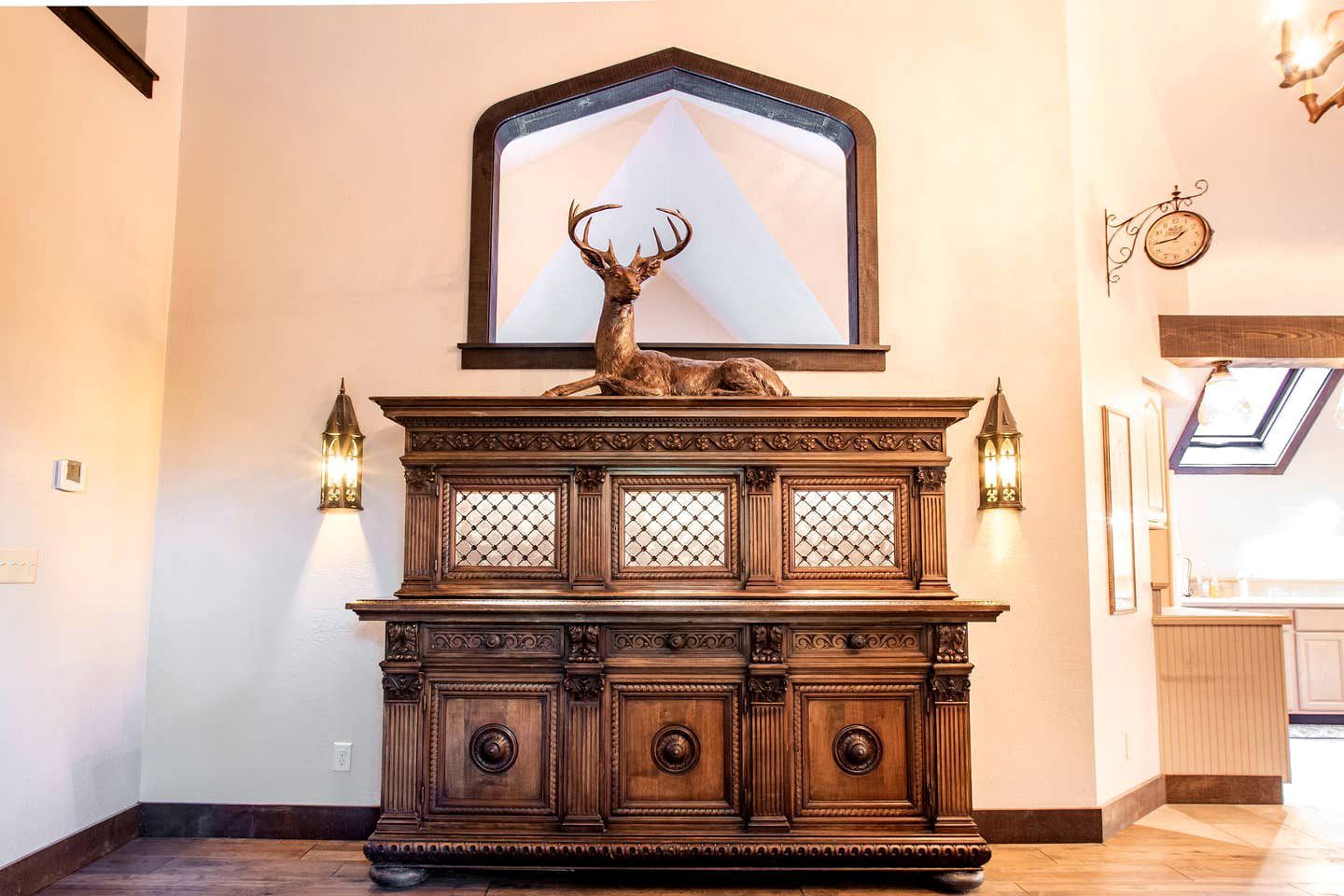 A wooden cabinet with a deer head sculpture, two wall-mounted sconces, and a large mirror above.
