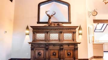 A wooden cabinet with a deer head sculpture, two wall-mounted sconces, and a large mirror above.