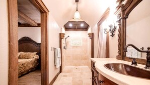 A narrow hallway leading to a bedroom with a bed, a bathroom with a sink and mirror, and a chandelier.