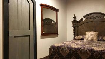 Quarto com uma cama, porta de madeira e espelho na parede.