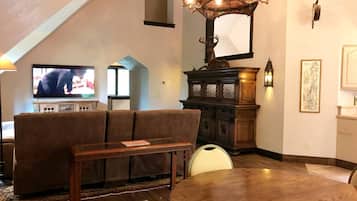 A living room with a sofa, a dining table, a chandelier, and a television.