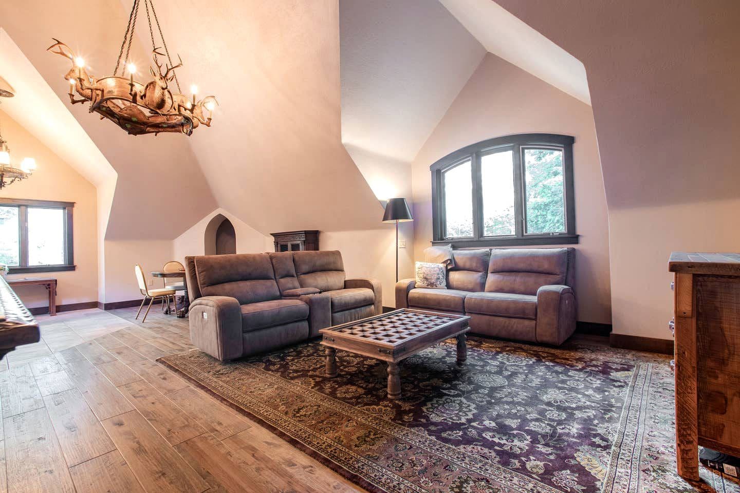 A spacious loft with a high ceiling, a grand chandelier, a piano, two sofas, a coffee table, and a large window.
