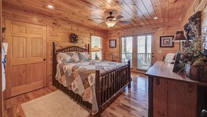 A wooden cabin bedroom with a bed, a ceiling fan, a desk, and a window. - Pristine 3-bedroom cabin with gorgeous views in Mineral Bluff (Mineral Bluff)