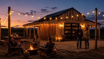 A rustic wooden barn with string lights, outdoor seating, and a fire pit.