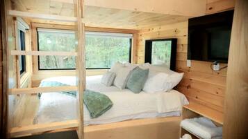A wooden cabin bedroom with a bed, pillows, a TV, and large windows.