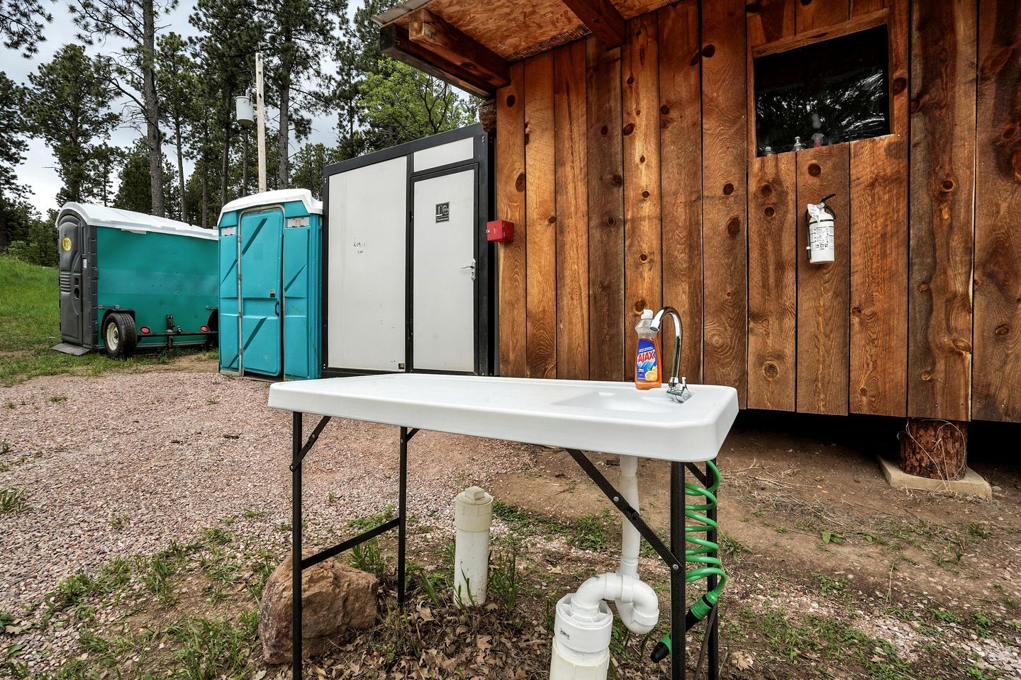 Ein tragbares Waschbecken mit Seifenspender, eine mobile Toilette und ein Holzhäuschen.