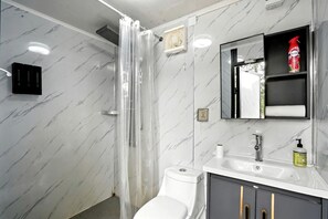 Un baño con ducha, inodoro, lavabo y un espejo con repisa superior.