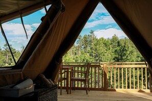 Alojamiento tipo tienda con terraza de madera, una silla y vistas a un bosque.